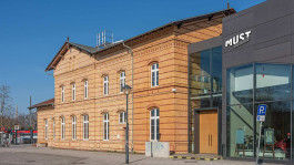 Das Museum für Stadt und Technik (MUST) in Ludwigsfelde mit historischem Backsteinbau und modernem Glas-Anbau. Ein digital erstelltes Mock-up zeigt den neuen »MUST«-Schriftzug auf der Fassade als Teil des Rebrandings.