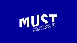 Neues Logo des Museums für Stadt und Technik (MUST) in Ludwigsfelde. Der weiße Schriftzug „MUST“ in Großbuchstaben ist leicht geneigt, darunter in kleineren Buchstaben der volle Name des Museums auf blauem Hintergrund.