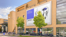 Großes Werbebanner für das Kreativquartier Potsdam an der Fassade des Potsdamer Hauptbahnhofs. Das Design zeigt eine Illustration mit einem kreativen Slogan und dem Logo „yarten. Kreativquartier“.