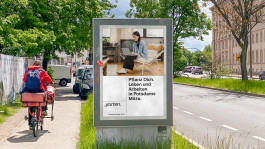 Freistehende Werbetafel für das Kreativquartier Potsdam an einer Straße, mit dem Motiv einer jungen Frau, die auf einem Laptop arbeitet, und dem Slogan „Pflanz Dich. Leben und Arbeiten in Potsdams Mitte.“.