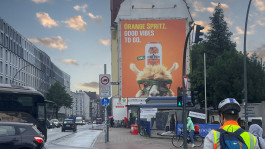 Großes Werbeposter für Somersby Orange Spritz mit einem Alpaka, das eine Getränkedose balanciert, an einer Hausfassade in Hamburg.